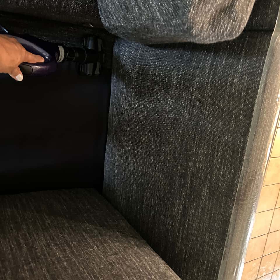 Handheld vacuum cleaning the crevice of a grey fabric sofa — Coastal Clean & Care LLC