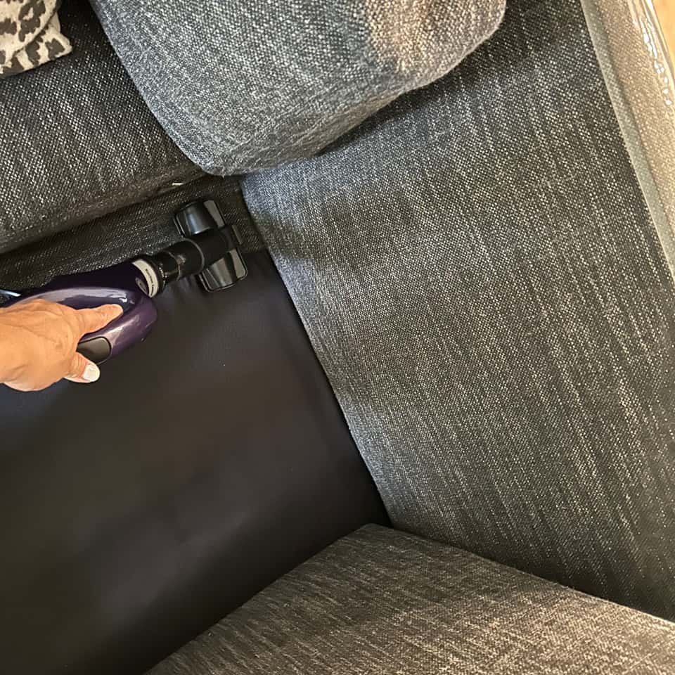 Vacuuming along the seam of a grey sofa cushion — Coastal Clean & Care LLC