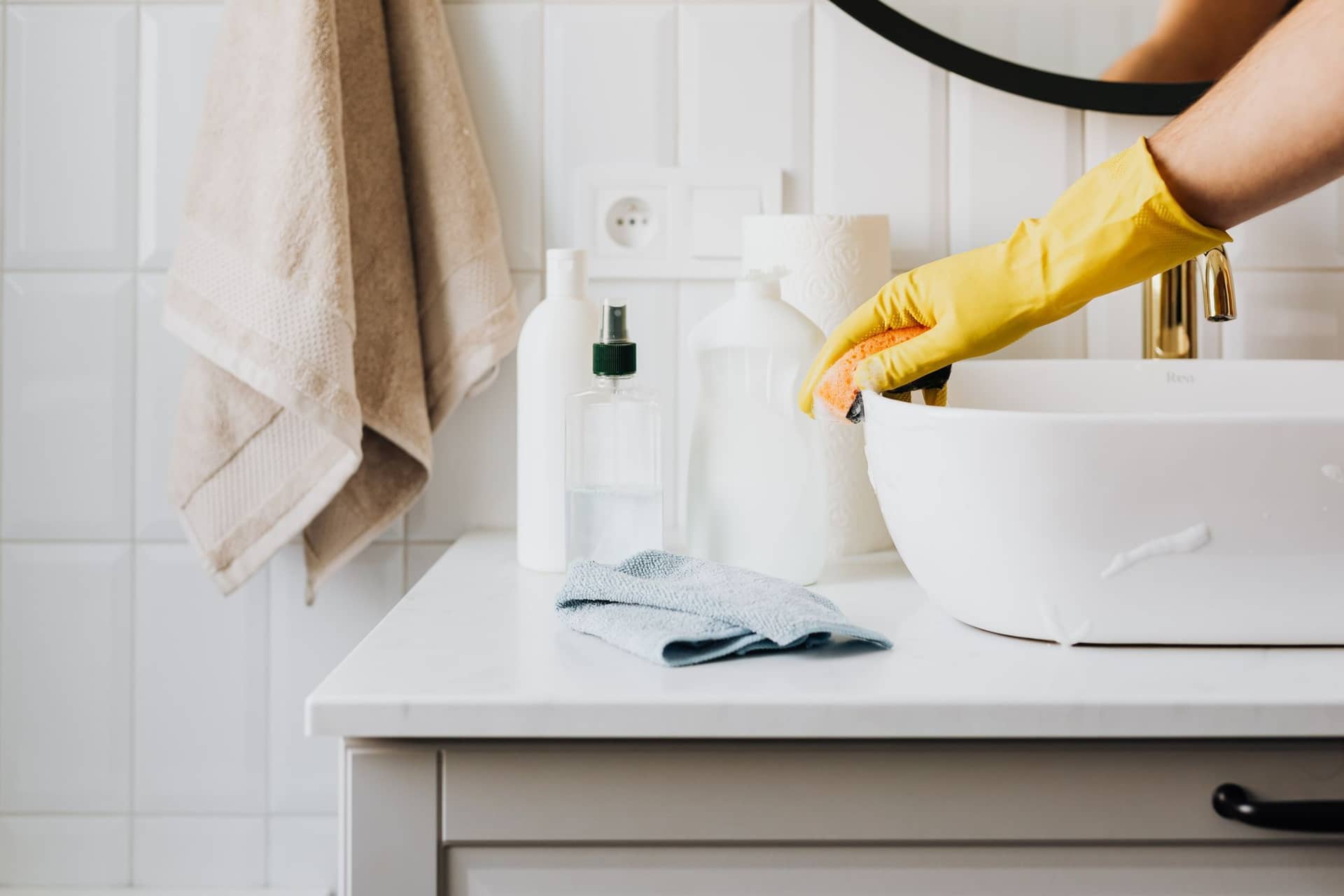 Cleaning supplies and a gloved hand wiping a bathroom counter